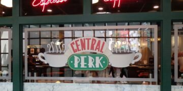 Neon red 'Espresso' and 'Cappuccino' signs in a cafe window above a Central Perk logo.